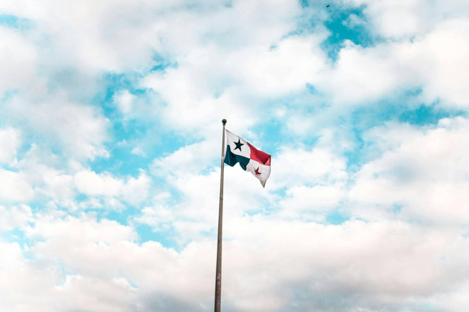 A Panama flag waving on a flagpole against a bright, cloudy blue sky.