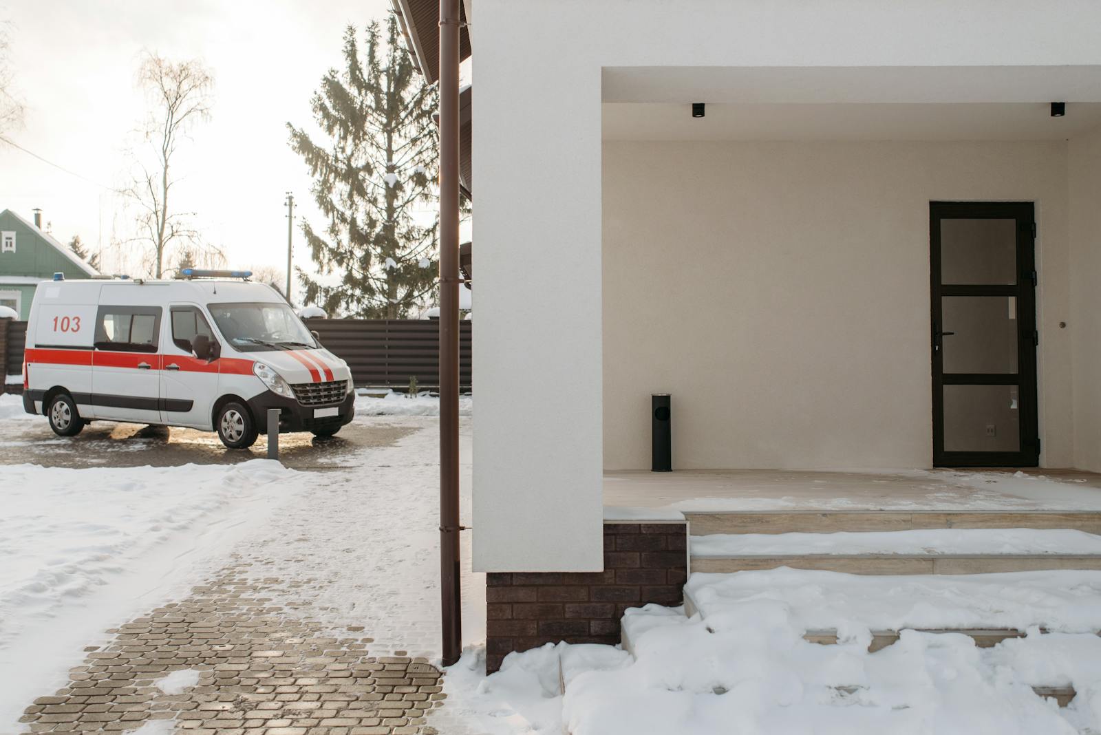 A parked ambulance near a snow-covered modern house during winter, displaying calm suburban life.
