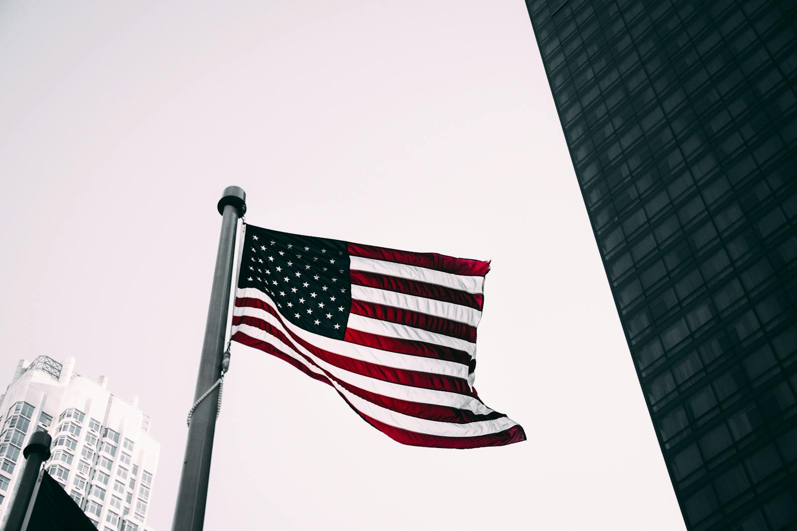 Low angle view of the American flag waving against modern skyscraper background.