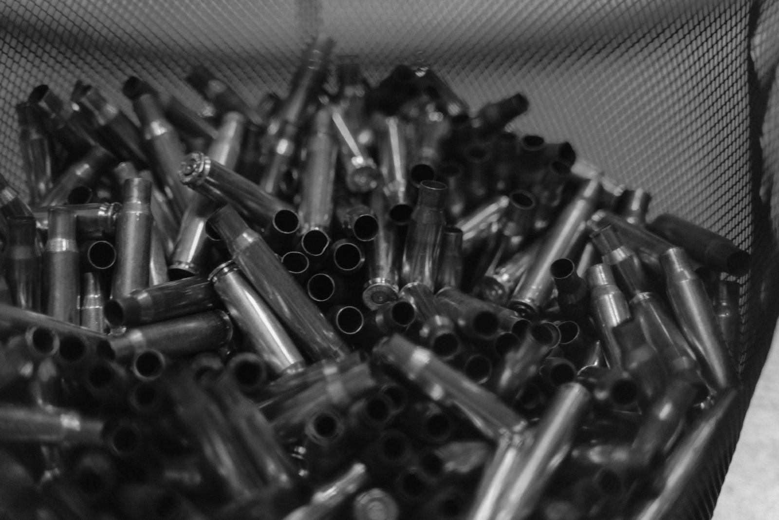 Black and white image of spent bullet casings in a container, emphasizing shooting and military themes.