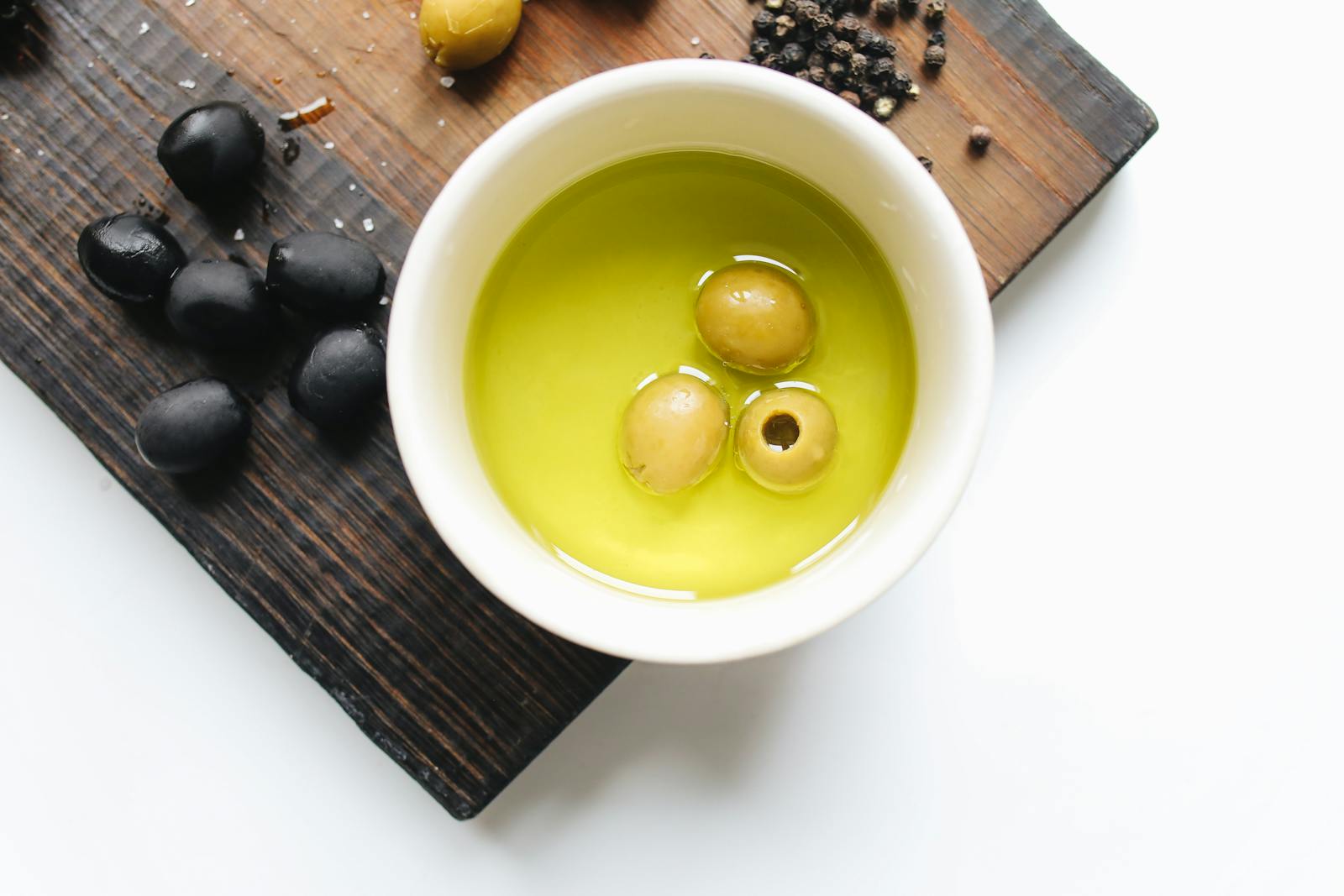 Top view of green olives in oil, black olives, and pepper on a cutting board.