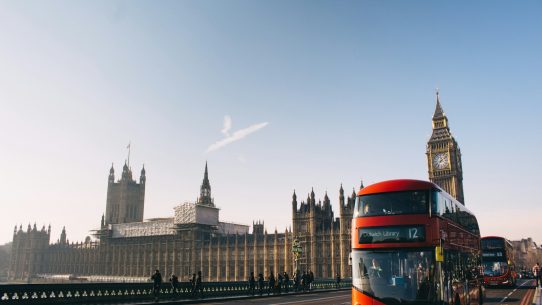 red double-decker bus passing Palace of Westminster, London during daytime