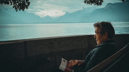 man sitting while holding a book watching on body of water
