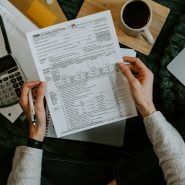 Hands holding tax forms with calculator and laptop.