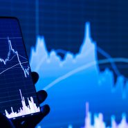 a person holding a cell phone in front of a stock chart