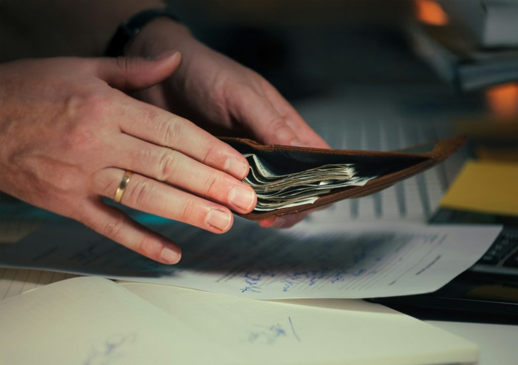 Hands holding cash in a wallet over papers.