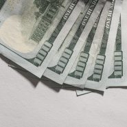 Several hundred dollar bills fanned out on a white surface