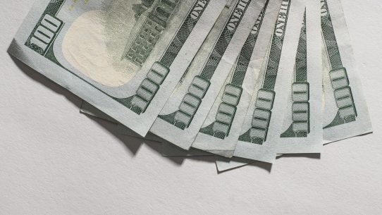 Several hundred dollar bills fanned out on a white surface