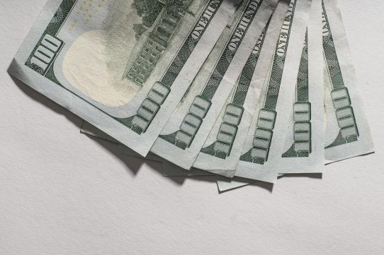 Several hundred dollar bills fanned out on a white surface