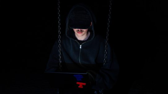 A figure is using a laptop in the dark.