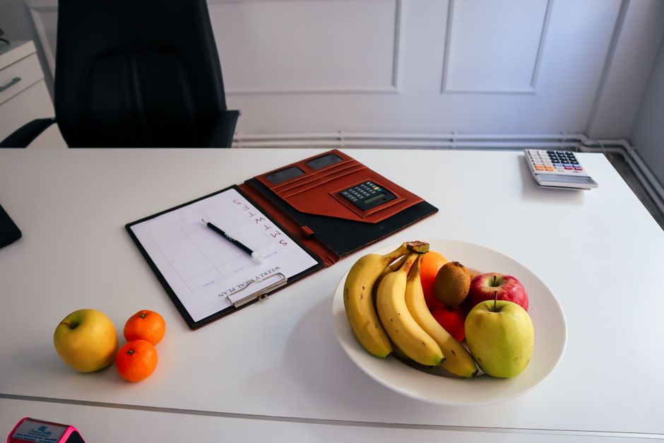 A neat office desk setup with fresh fruits, a planner, and a calculator for organized work days.