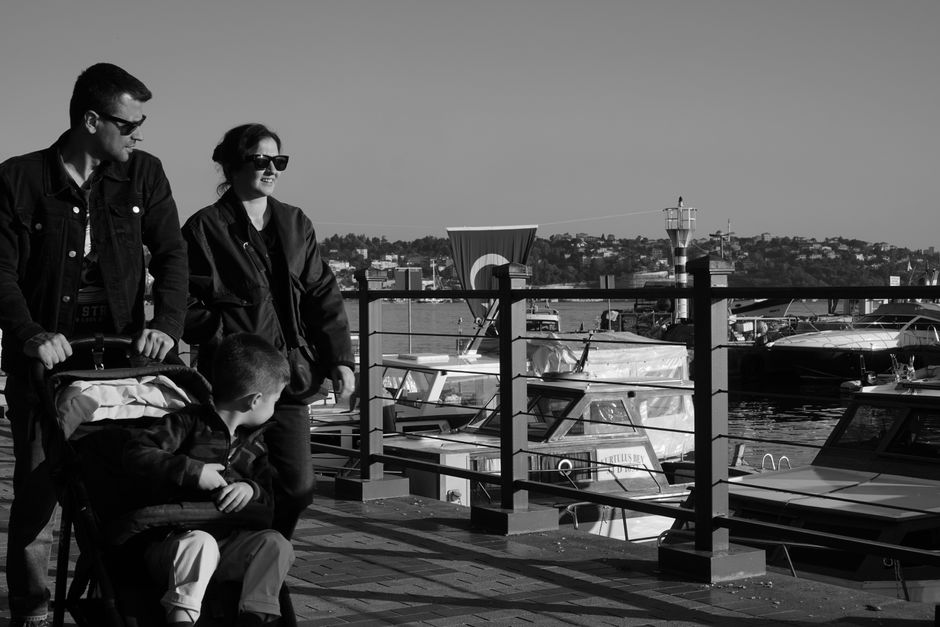 Black and white photo of a family walking by a marina, enjoying a sunny day.
