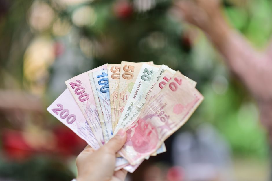 A hand holding multiple Turkish Lira banknotes in an outdoor setting, showcasing various denominations.