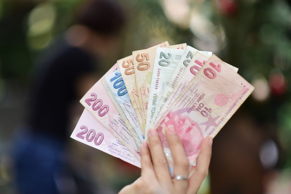 A hand holding various Turkish Lira banknotes with a blurred outdoor background.