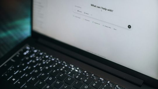 A laptop displays "what can i help with?"