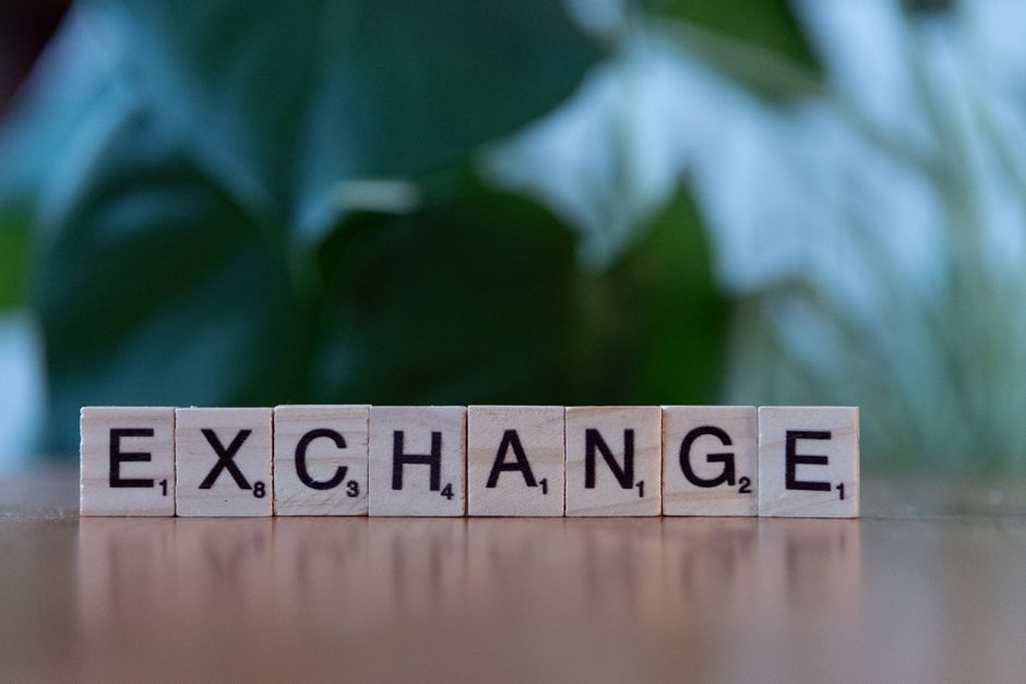 Wooden blocks spelling'exchange' on a table with a blurred green background.