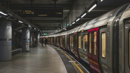 A London Underground train at a platform with a digital arrival sign