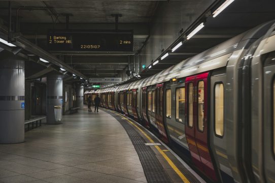 A London Underground train at a platform with a digital arrival sign