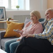 Elderly couple smiling and enjoying time together on a cozy living room sofa.
