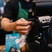 Close-up of a barista processing a payment using a card reader in a café setting.