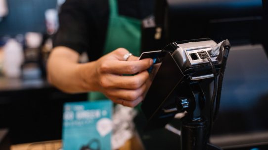 Close-up of a barista processing a payment using a card reader in a café setting.