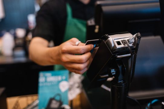 Close-up of a barista processing a payment using a card reader in a café setting.