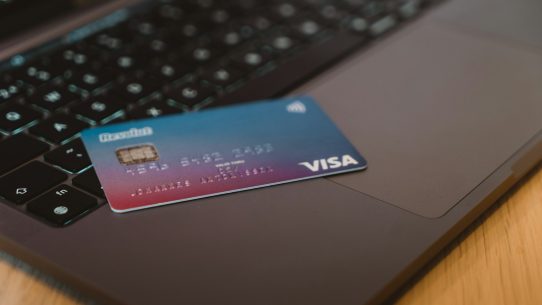 A blue and red gradient debit card resting on a dark laptop keyboard